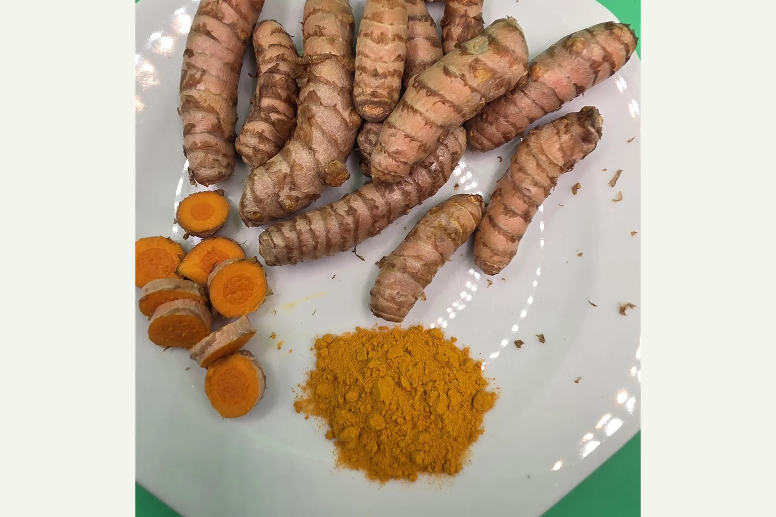 Kurkumarhizome, orangefarbene Schnittflächen und Pulver auf einem weißen Teller